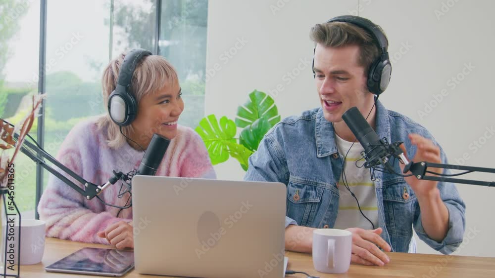 Couple wearing headphones live streaming podcast using laptop and digital tablet- shot in slow motion