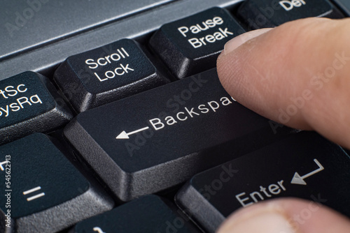 Finger presses backspace key on computer keyboard photo