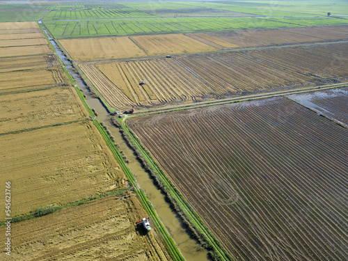 Aerial drone view of machines tractors harvesting vast rice fields. Industrial agriculture. Tagus Estuary Natural Reserve in Lisbon, Portugal. Native Rice of Portugal. River, water, wetlands.
 photo