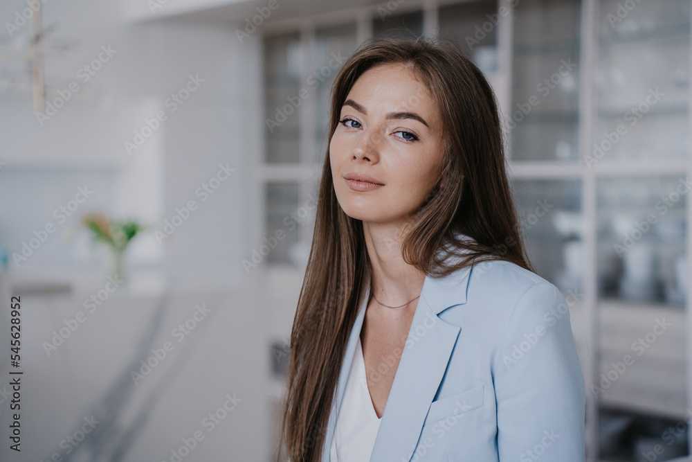 Portrait of gorgeous blonde Caucasian young woman in light blue jacket looking at camera confidently over blurry interior with empty space. Mockup, beautiful successful people. Candid female at home. Portrait of gorgeous blonde Caucasian young woman in light blue jacket looking at camera confidently over blurry interior with empty space. Mockup, beautiful successful people. Candid female at home.