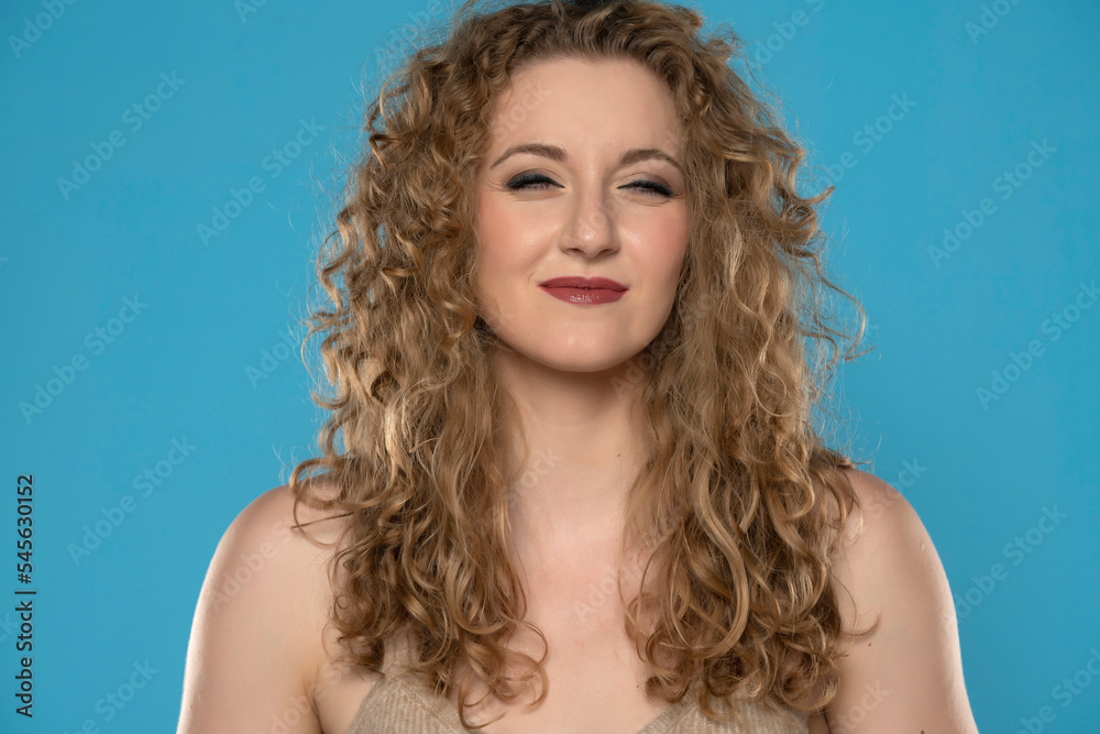 Portrait of curious curly-haired blond woman peering into distance on blue background.