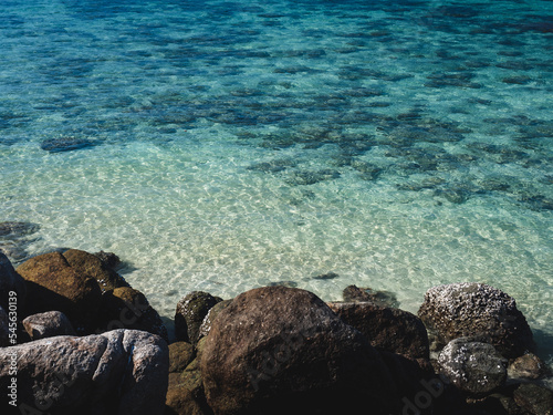 Scenic view of Sunset Beach, Koh Lipe Island. Rocky coastline against crystal clear turquoise sea with coral reef transparent shallow water. Satun, Thailand. Natural background with copy space.