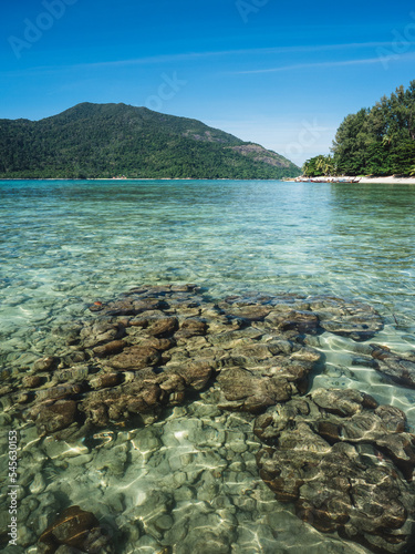 Scenic view of Sunset Beach, Koh Lipe Island. Crystal clear shallow water with coral reef transparent against summer blue sky and Koh Adang Island background. Satun, Thailand.