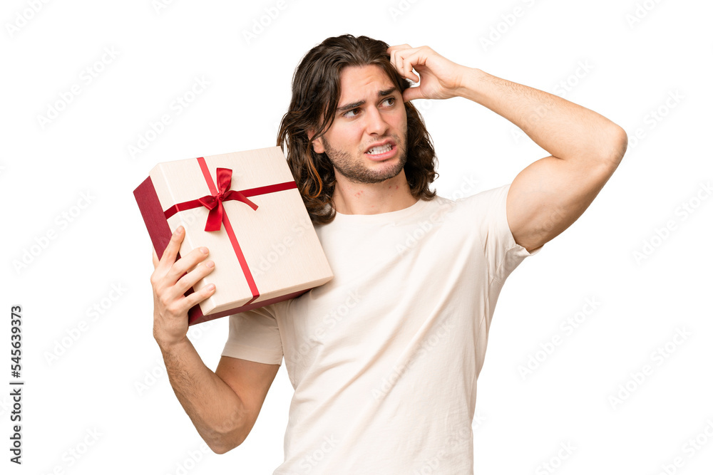 Young handsome man holding a gift over isolated background having doubts and with confuse face expression Young handsome man holding a gift over isolated background having doubts and with confuse face expression