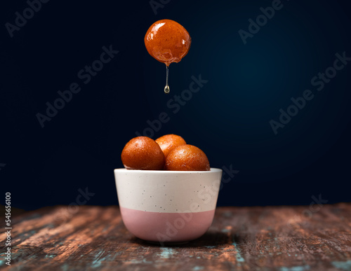 Gulab Jamun served in a bowl with pouring sweet syrup.