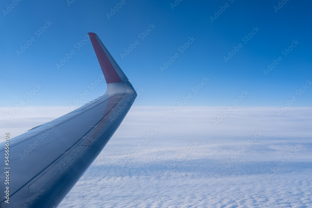 The wing of the plane against the background of white wavy clouds and the stratosphere. Background of blue sky with fluffy dense clouds. Sky gradient. The concept of travel.