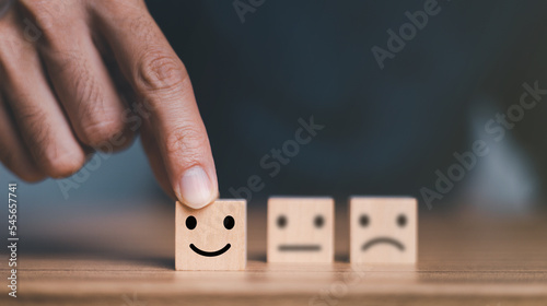 Close up customer hand choose smile face and blurred sad face icon on wood cube, Service rating, Customer service evaluation and satisfaction survey concepts.