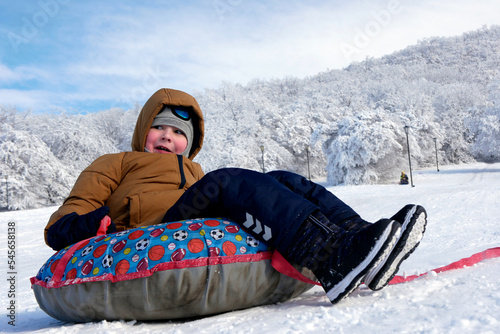 Cheerful child boy riding on snow tubing down hill. Winter joy and outdoor actovity
