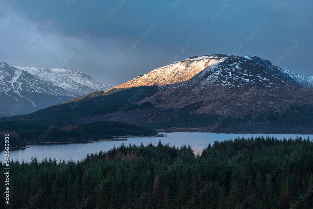 Majestic beautiful Winter sunrise panorama landscape image of glowing light on mountain range and peaks beyod Loch Tulla in Scottish Highlands
