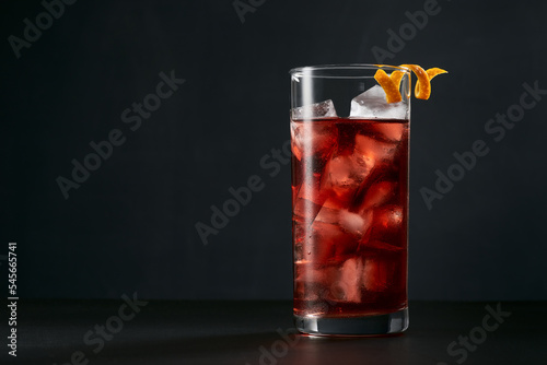 Negroni cocktail in highball or collins glass with orange peel on a dark background.