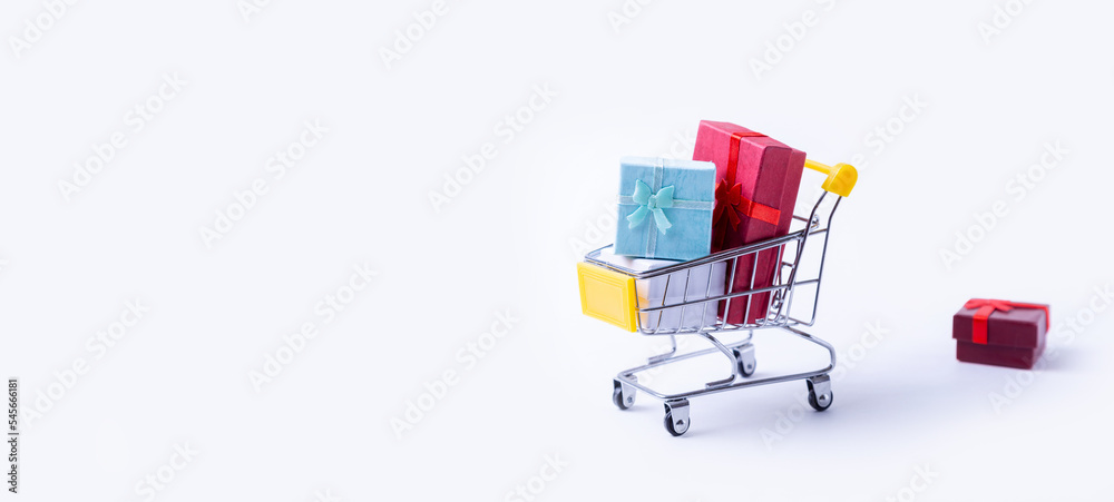 Miniature cart with gifts on a white background. Holidays shopping concept. Holidays New Year, Christmas, birthday. Copy space. Selective focus, close-up.