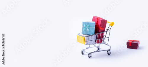Miniature cart with gifts on a white background. Holidays shopping concept. Holidays New Year, Christmas, birthday. Copy space. Selective focus, close-up.