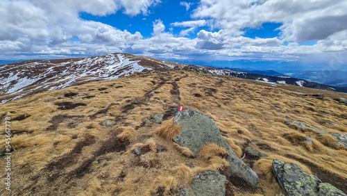 Directional path mark with Austrian flag painted on rock near Ladinger Spitze, Saualpe, Carinthia, Austria, Europe. Hiking trail on alpine meadow in Austrian Alps. Hills covered in snow, early spring photo