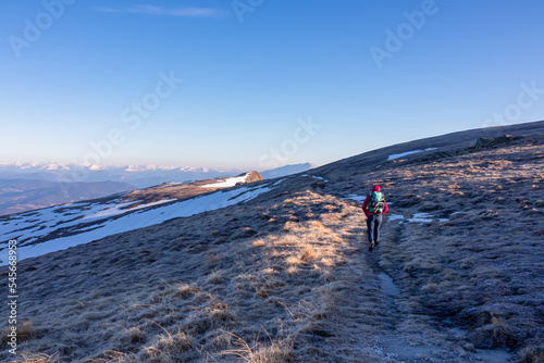 Woman hiking on frozen alpine meadow from Ladinger Spitz to Gertrusk, Saualpe, Lavanttal Alps, Carinthia, Austria, Europe. Morning frost on cold early spring day. Trekking in the Austrian Alps
