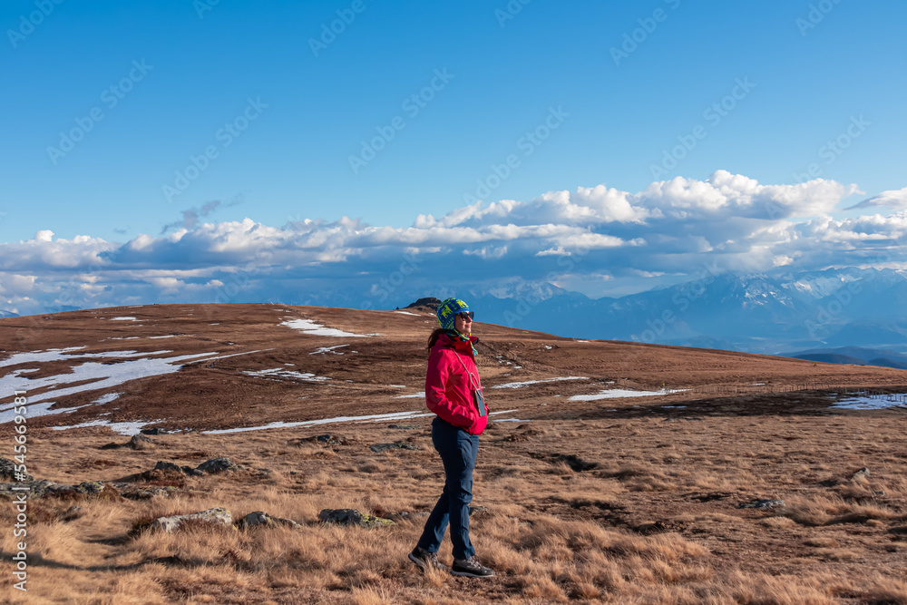 Woman with ear flap hat standing on alpine meadow with scenic view on Grosser Sauofen (Ebersteiner Sau), Saualpe, Lavanttal Alps, Carinthia, Austria, Europe. Slow trekking in Austrian Alps
