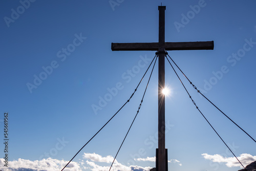 Silhouette of summit cross of mountain peak Zingerle Kreuz, Saualpe, Lavanttal Alps, Carinthia, Austria, Europe. Hiking trail Wolfsberg. Sunbeams creating a sun star, dispersion of light photography photo