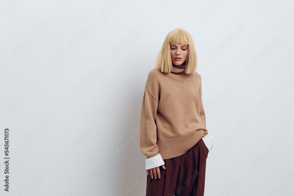 Fototapeta premium Horizontal photo, a woman on a white background in a beige sweater and brown trousers with beautiful blond hair is standing