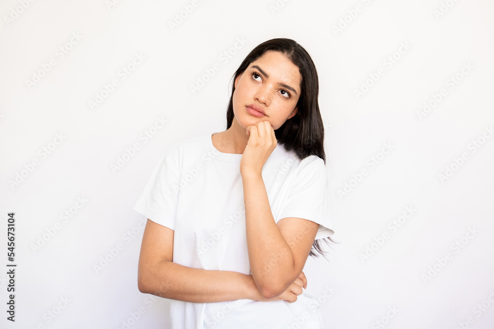 Portrait of confident young woman thinking over idea. Caucasian lady wearing white T-shirt standing with hand on chin and looking away over white background. Thinking or planning concept Portrait of confident young woman thinking over idea. Caucasian lady wearing white T-shirt standing with hand on chin and looking away over white background. Thinking or planning concept