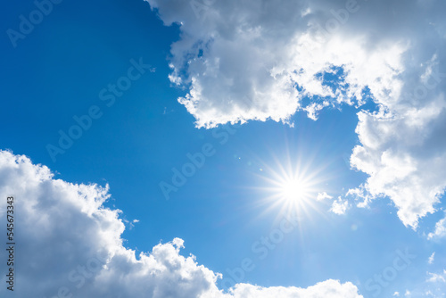 The sun shines with blue sky between soft clouds