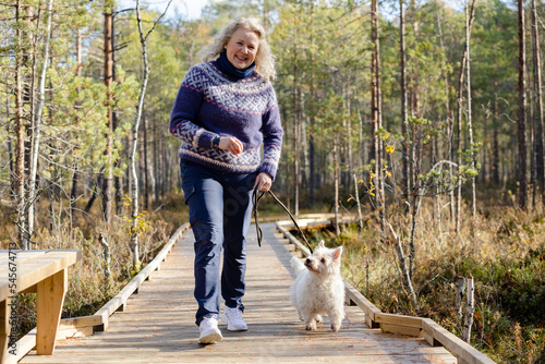 Woman with West Highland white terrier walking on forest trail