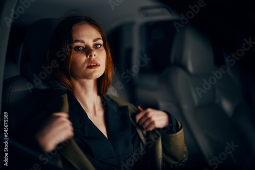 a stylish, luxurious woman sits in a black car at night in the passenger seat, and adjusts her coat thoughtfully looking © SHOTPRIME STUDIO