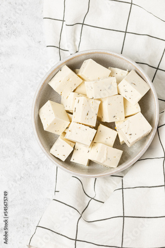 Tofu soy cheese or paneer or feta cheese cubes in a ceramic bowl on a checkered napkin isolated top view