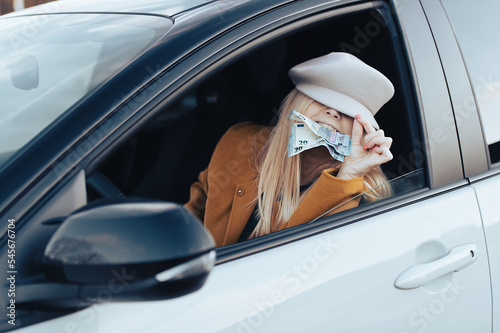 middle aged woman sitting in a car and holding euro banknotes in her teeth, cost of living concept © Zelma
