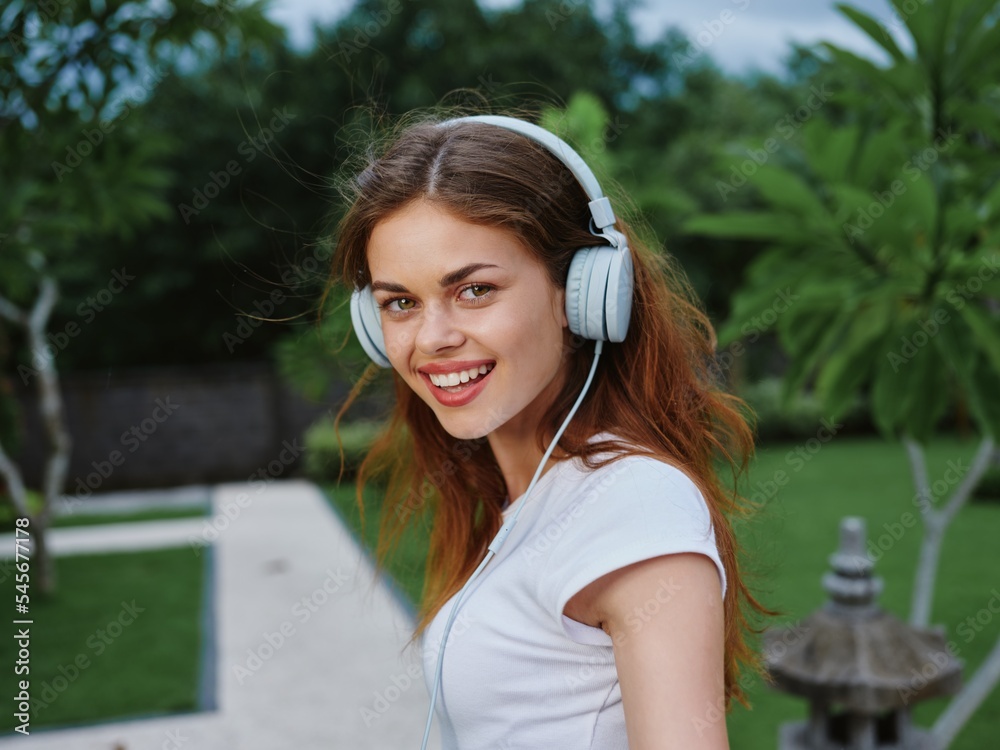 Girl wearing headphones in a white T-shirt listening to music and walking down the street, smile, follow me Girl wearing headphones in a white T-shirt listening to music and walking down the street, smile, follow me