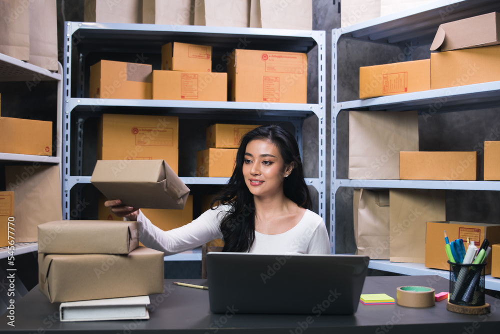 A female employee is packing parcels and checking customer addresses with a laptop to deliver goods. She owns a business and runs a store to sell online, shipping and startup concept A female employee is packing parcels and checking customer addresses with a laptop to deliver goods. She owns a business and runs a store to sell online, shipping and startup concept