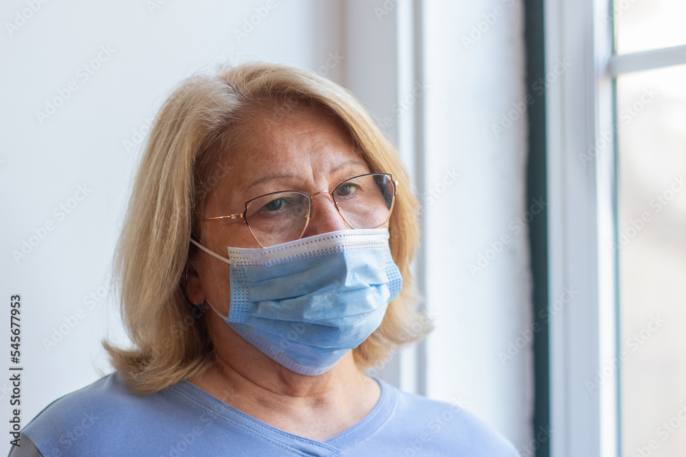 Close-up of Caucasian woman in protective mask on her face. Serious woman taking care of her health staying at home for self-isolation. Health care and senior people during Covid pandemic concept