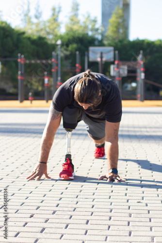 Portrait of man with disability training his legs outdoors. Caucasian man doing sports on stadium holding his hands on pavement and stretching. Sport activity of people with disability concept
