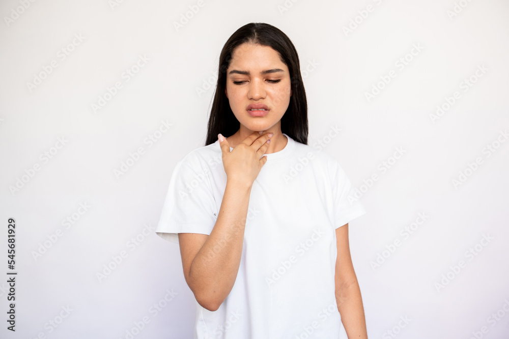 Portrait of unhappy young woman feeling pain in throat. Caucasian lady wearing white T-shirt touching neck over white background. Pulmonary diseases concept Portrait of unhappy young woman feeling pain in throat. Caucasian lady wearing white T-shirt touching neck over white background. Pulmonary diseases concept