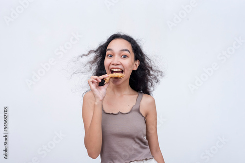 A young asian woman eagerly chomps on a sweet chili chicken wing. Fastfood concept. Isolated on a light background. photo