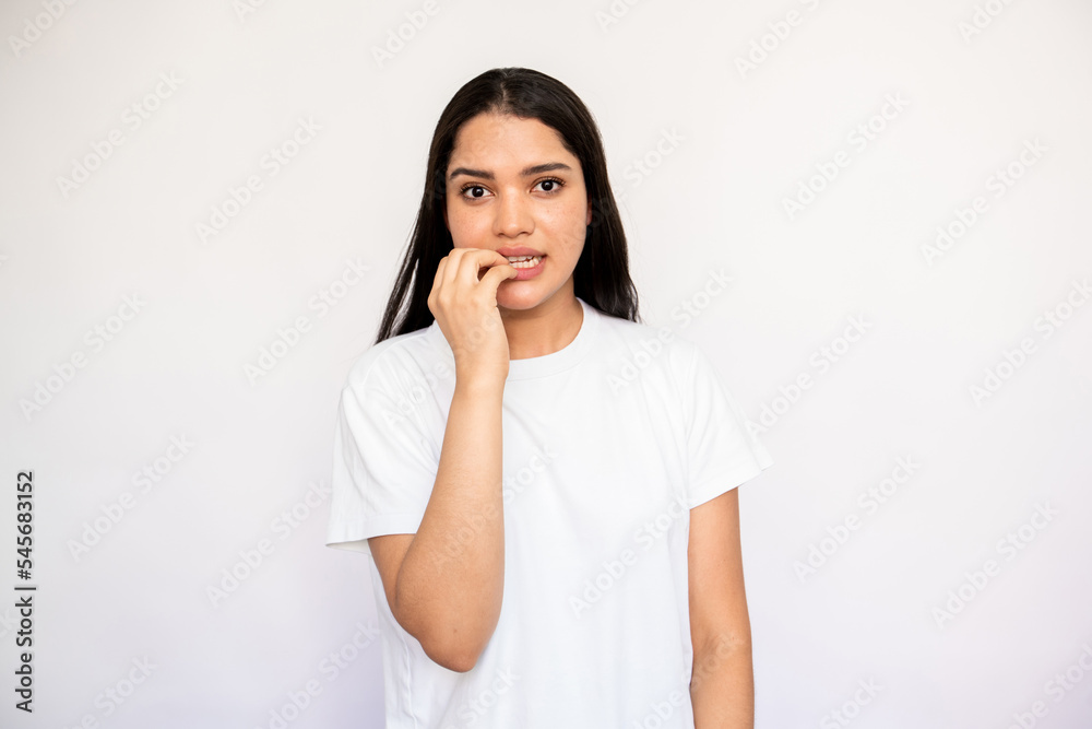 Portrait of nervous young woman biting nails in anxiety over white background. Caucasian lady wearing white T-shirt feeling worried and uneasy. Stress or fear concept Portrait of nervous young woman biting nails in anxiety over white background. Caucasian lady wearing white T-shirt feeling worried and uneasy. Stress or fear concept