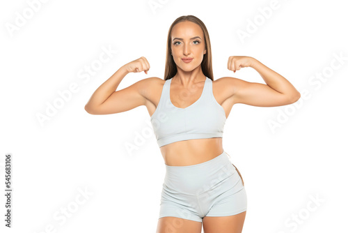 young sports woman with long hair in a shorts and top showing biceps on a white background