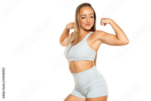 young sports woman with long hair in a shorts and top showing biceps on a white background