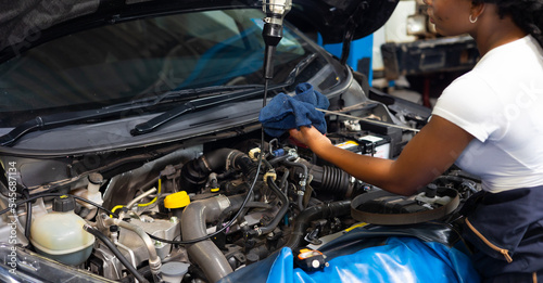 African female auto mechanic worker checking oil level in car engine at Car Service station. Car maintenance and auto service garage concept.