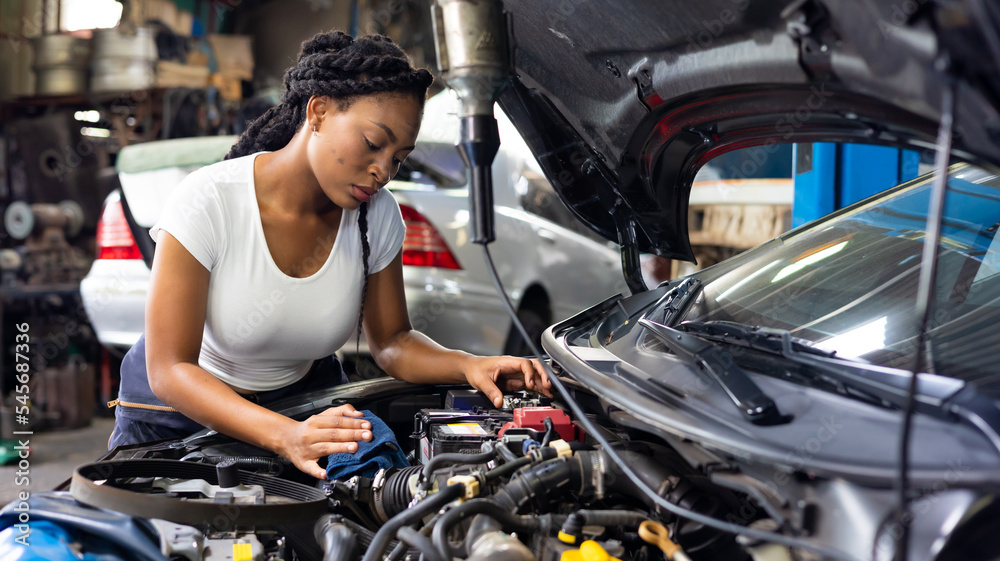 Charge electric power to ca battery by charging jumper cables. African  mechanic female uses  multimeter voltmeter to check voltage level in car battery at car service and maintenance garage.