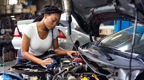 Charge electric power to ca battery by charging jumper cables. African mechanic female uses multimeter voltmeter to check voltage level in car battery at car service and maintenance garage.