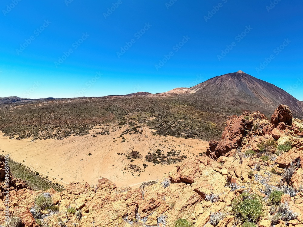 Scenic view on volcano Pico del Teide seen from Riscos de la Fortaleza, Mount El Teide National Park, Tenerife, Canary Islands, Spain, Europe. Hike via La Canada de los Guancheros dry desert plain
