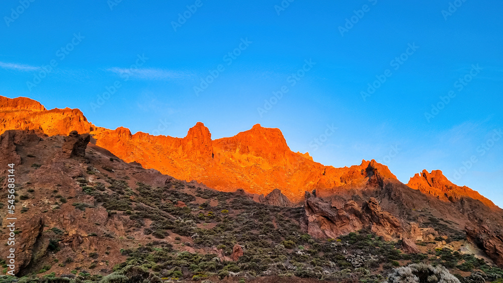 Scenic view on rock formations during sunrise near volcano Pico del Teide, Mount Teide National Park, Tenerife, Canary Islands, Spain, Europe. First sunbeams touching mountain peaks turning fire red
