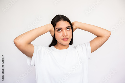 Portrait of ignorant young woman covering ears with hands over white background. Caucasian lady wearing white T-shirt protecting ears from noise. Ignorance concept © KAMPUS