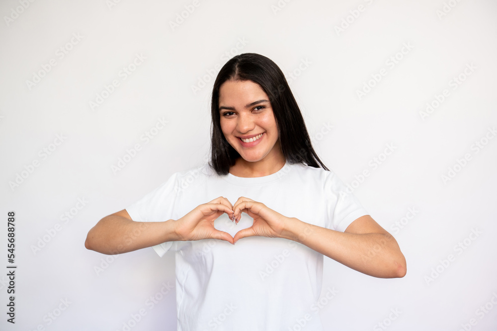 Portrait of happy young woman making heart gesture over white background. Caucasian lady wearing white T-shirt showing love or gratitude symbol. Love and admiration concept Portrait of happy young woman making heart gesture over white background. Caucasian lady wearing white T-shirt showing love or gratitude symbol. Love and admiration concept