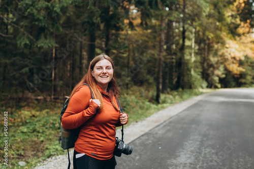 Stylish Tourist Woman hiking on footpath in autumn forest. Happy redhead person in active trekking clothes walking on nature backgraund. Travel and active lifestyle concept.