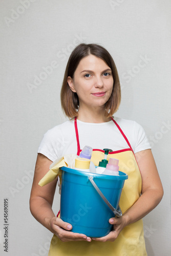 The girl holds a bucket and cleaning products in her hands