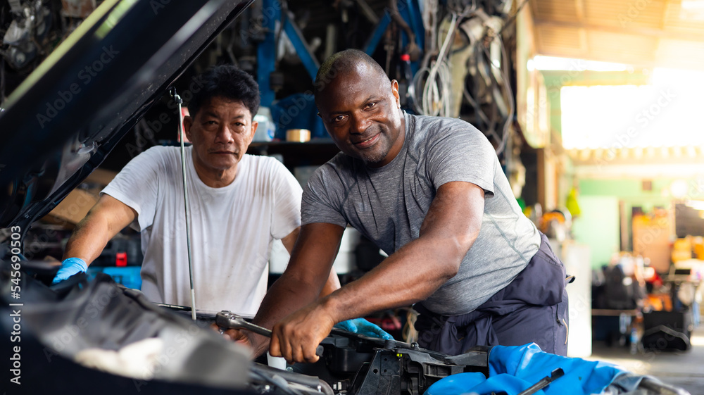 Professional Mechanical Engineer Asian senior old man and young man team Working under car at Car maintenance and auto service garage. African american black people. Unity professional teamwork