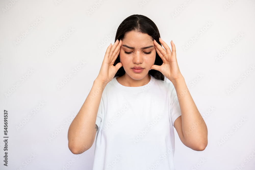 Portrait of stressed young woman suffering from headache over white background. Caucasian lady wearing white T-shirt rubbing aching temples. Exhaustion and migraine concept Portrait of stressed young woman suffering from headache over white background. Caucasian lady wearing white T-shirt rubbing aching temples. Exhaustion and migraine concept