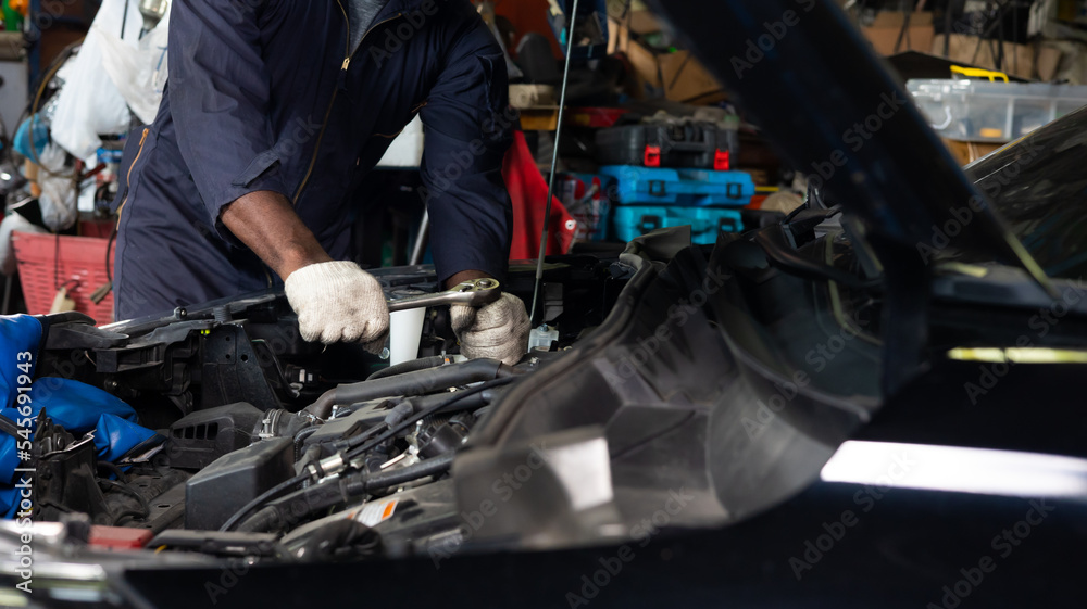 Close up hand black male mechanic repairs car in garage. Car maintenance and auto service garage concept. Close up hand black male mechanic repairs car in garage. Car maintenance and auto service garage concept.