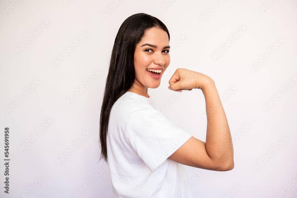 Portrait of happy young woman showing muscle on white background. Caucasian lady wearing white T-shirt showing fit body. Strength and fitness concept Portrait of happy young woman showing muscle on white background. Caucasian lady wearing white T-shirt showing fit body. Strength and fitness concept