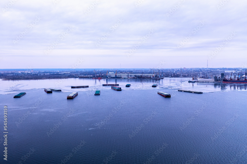 A cargo ships standing on a frozen river. Freight transportation concept, import export and business logistics, aerial view in winter. Nikolaev, Ukraine A cargo ships standing on a frozen river. Freight transportation concept, import export and business logistics, aerial view in winter. Nikolaev, Ukraine